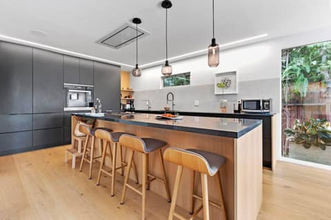 Experience the excitement of our spacious, fully-equipped modern kitchen! The island is perfect for enjoying a relaxed dinner or entertaining guests while you cook. The vibrant green view from outside creates a stunning contrast with the cabinets.