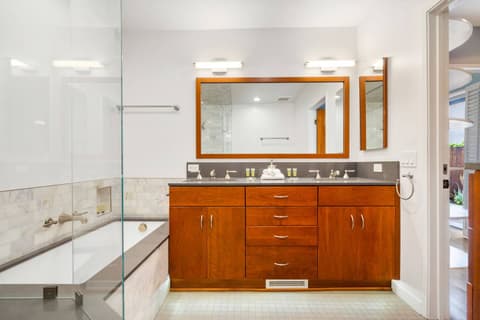 Elegant bathroom featuring a luxurious soaking tub, glass-enclosed shower, and dual-sink vanity with rich wood cabinetry. Bright and modern, it offers a spa-like experience, perfect for relaxation and comfort during your stay.