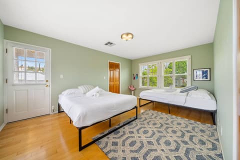 Spacious bedroom with two comfortable beds, large windows for natural light, and a small private balcony to enjoy fresh air. Features a cozy rug and warm decor, perfect for relaxation and a restful stay.