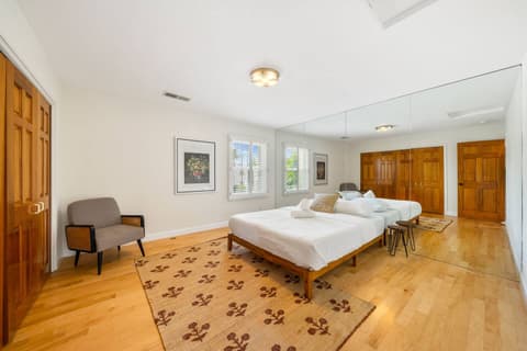 Spacious bedroom featuring a comfortable bed, mirrored walls, and large windows that fill the room with natural light. Decorated with warm tones and a cozy rug, it provides a relaxing and inviting space for a restful stay.