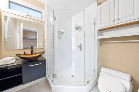 Compact and stylish bathroom featuring a unique vessel sink, a modern glass-enclosed shower, and sleek cabinetry. Bright and functional, it offers a cozy yet elegant space for your daily routines.